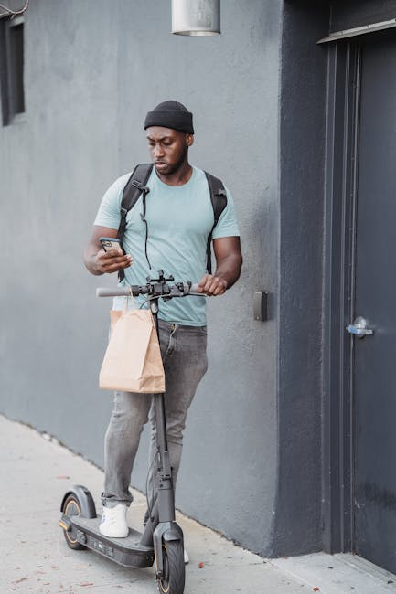 A man standing on an electric scooter outdoors, holding a brown paper bag in one hand and a bouquet of fresh flowers in the other. The bouquet features a vibrant assortment of roses, lilies, and other